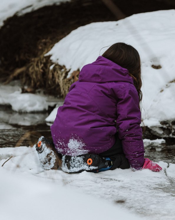 Image features a child kneeling by a frozen creek.