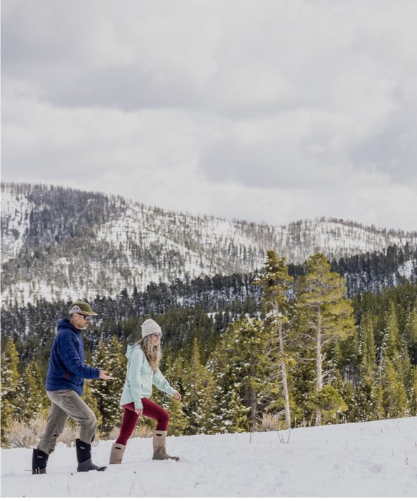 Image features a man and woman walking in their Bogs with 2 dogs. 