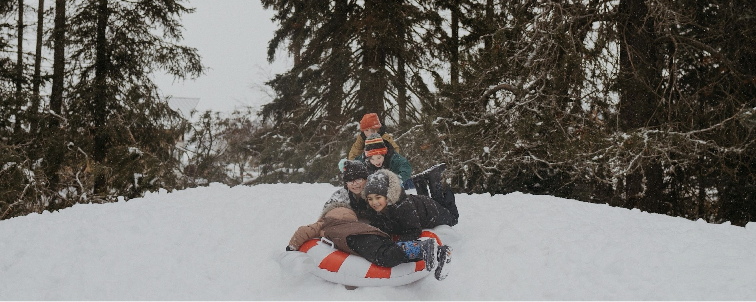 Image features a group of kids dog-piling on a snow intertube. 