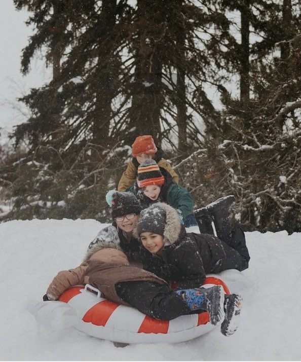 Image features a group of kids dog-piling on a snow intertube. 