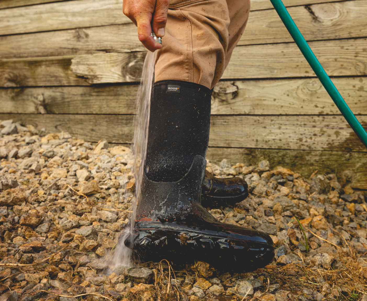 The image shown is a closeup image of our Men's Classic Seamless boot tall walking through mud with a tractor in the background.