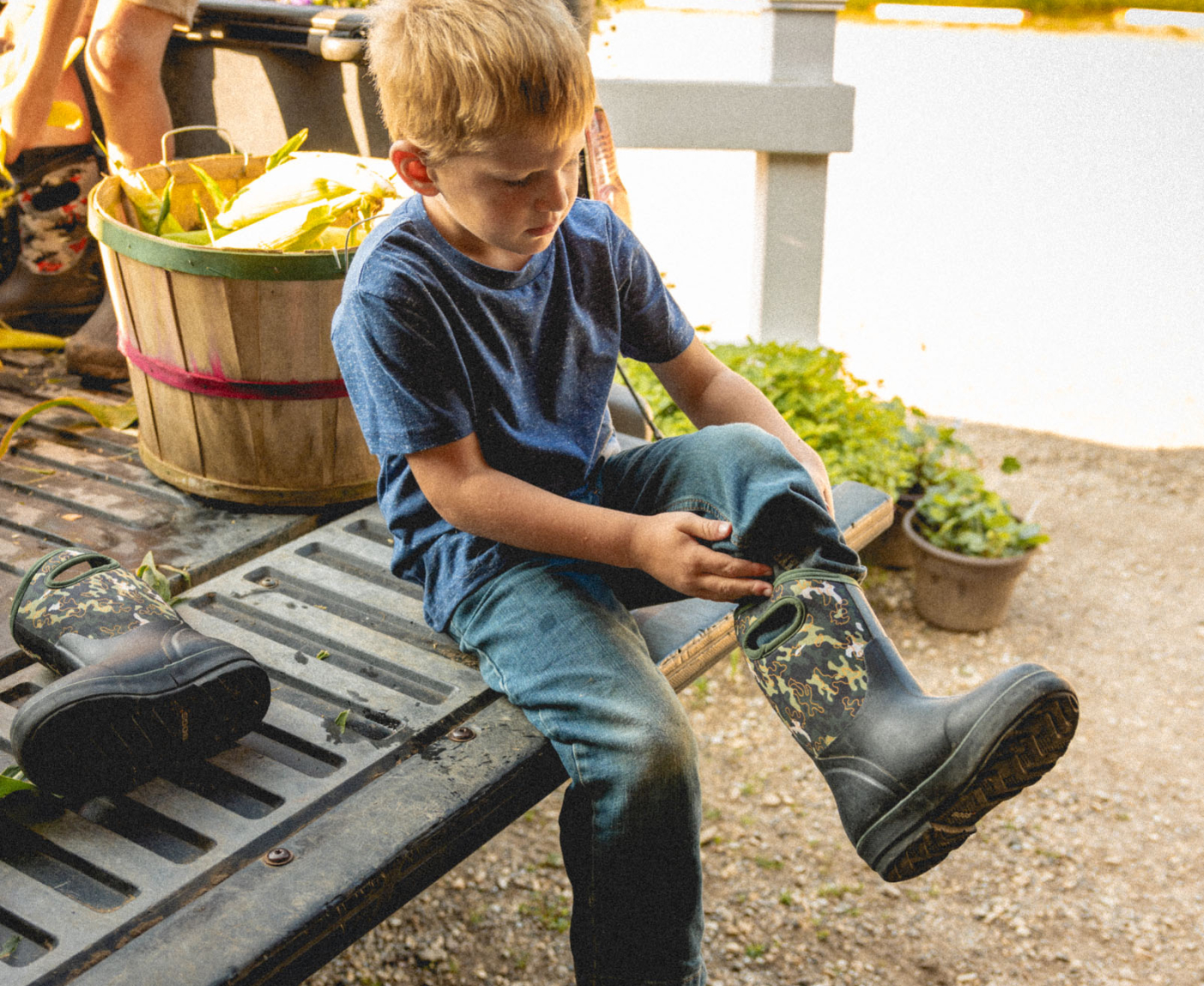 Shop our Kids' Seamless boots. The image shown is a kid pulling on his Neo-Classic boots on the back of a pick-up truck