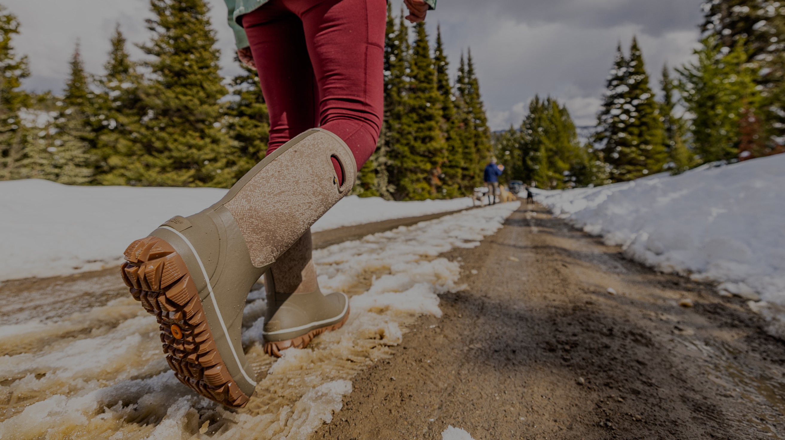 The image shown is a woman walking down a snowy muddy road in her winter boots.  The boots she is wearing are our Women’s Whiteout Faded waterproof winter boots in taupe. Shop now.