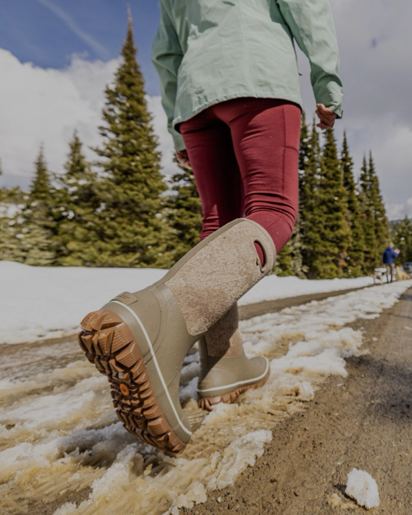 The image shown is a woman walking down a snowy muddy road in her winter boots.  The boots she is wearing are our Women’s Whiteout Faded waterproof winter boots in taupe. Shop now.