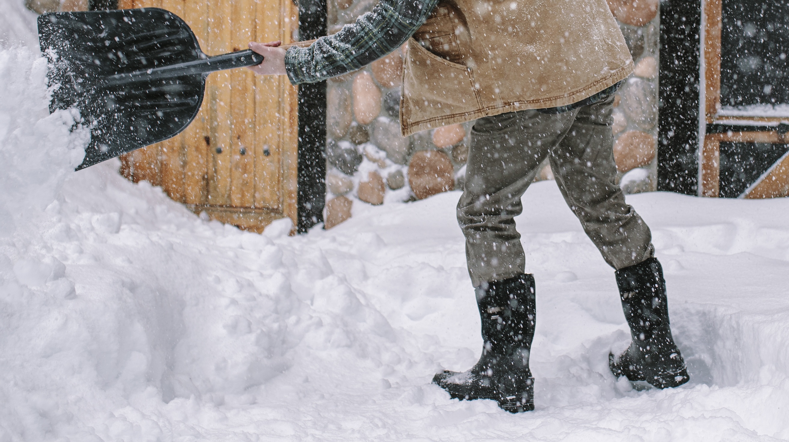 The image shown is a man shoveling snow outside of their cabin. Shop our top Men’s winter boots.